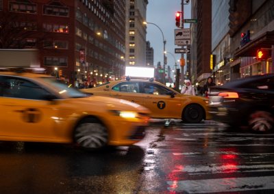 A,Taxi,Speeds,Across,A,Wet,Roadway,While,Blurred,Cars
